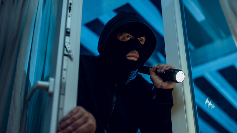 robber wearing a face mask and hoodie entering a house while holding a torch