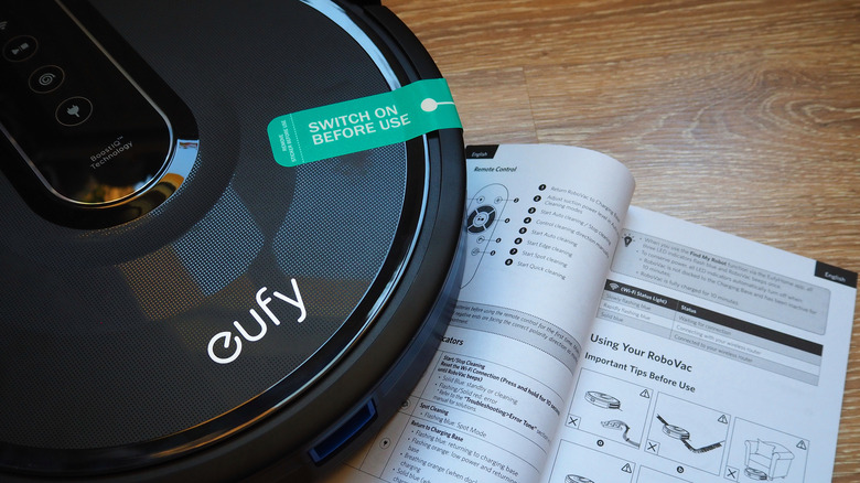 A Eufy robot vacuum placed next to its instruction manual.