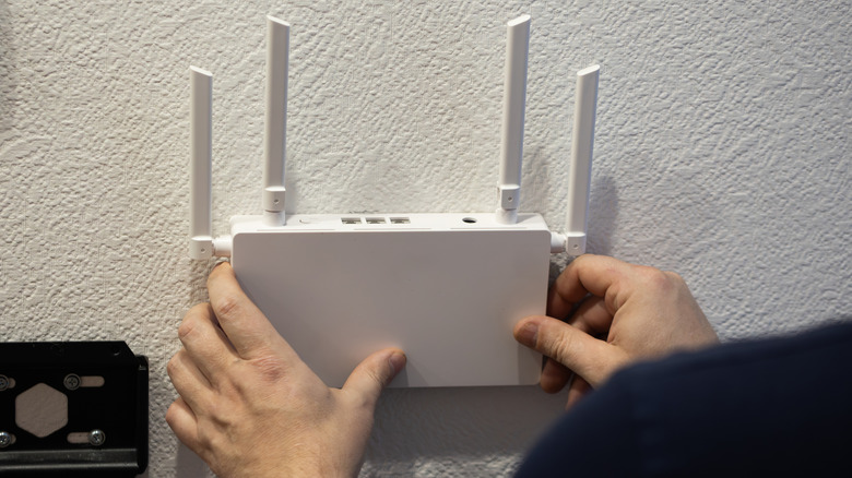 person installing a white wireless router with four antennas on a white wall