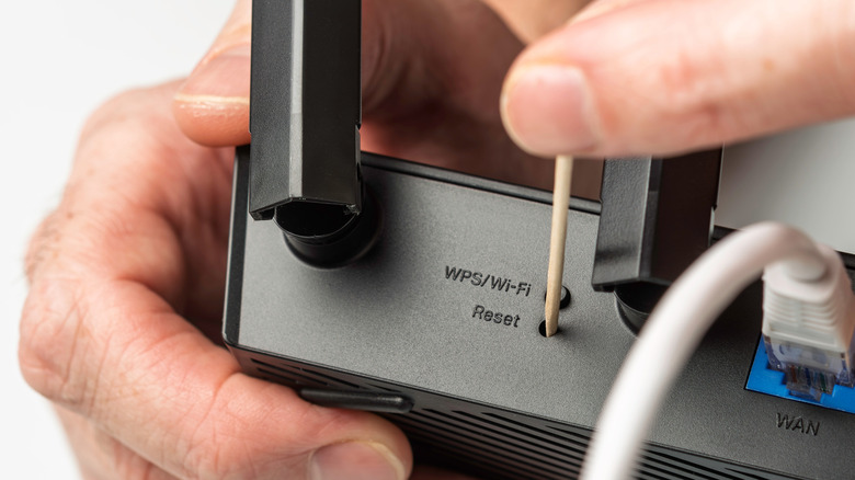 person using a toothpick to press the reset button on a router