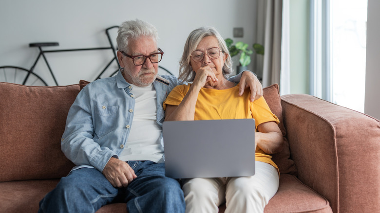 An older couple looking at a laptop on the couch.