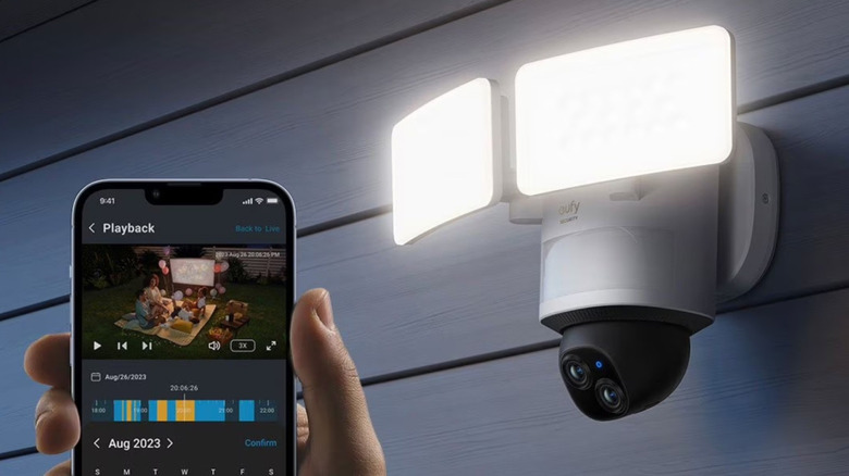 A person holding a phone displaying the Eufy app next to the Eufy E340, which is mounted to the exterior of a home.