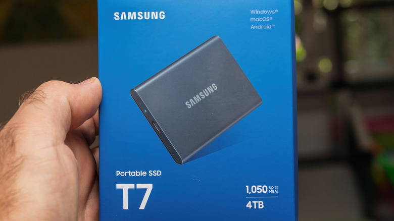 Hand holding Samsung T7 portable SSD retail box showing storage capacity and speed details.