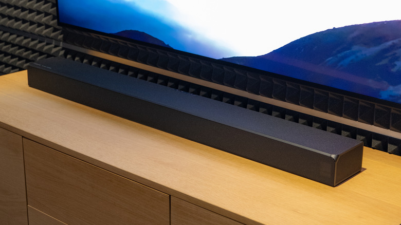 Samsung soundbar placed on a wooden TV stand below a television screen.
