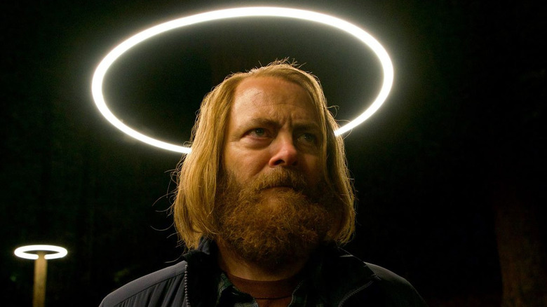 Nick Offerman standing under glowing circular lights at night, wearing a jacket and plaid shirt in a dark forest setting from the series Devs.