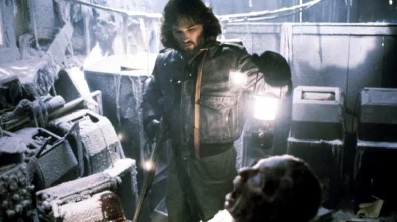 Kurt Russell as MacReady looking at a frozen body in The Thing