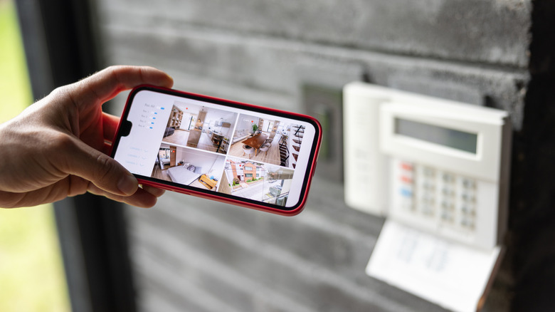 Person holding phone in front of home security keypad.