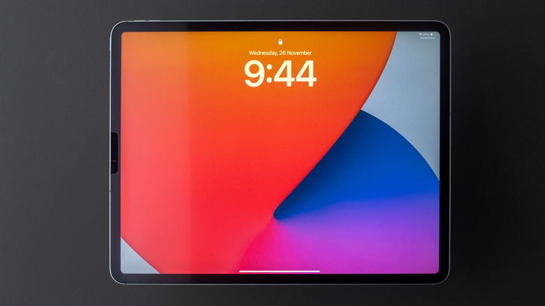 A closeup of a black Apple iPad, the device is displaying the lock screen which has a very colorful background of oranges, blues, and purples