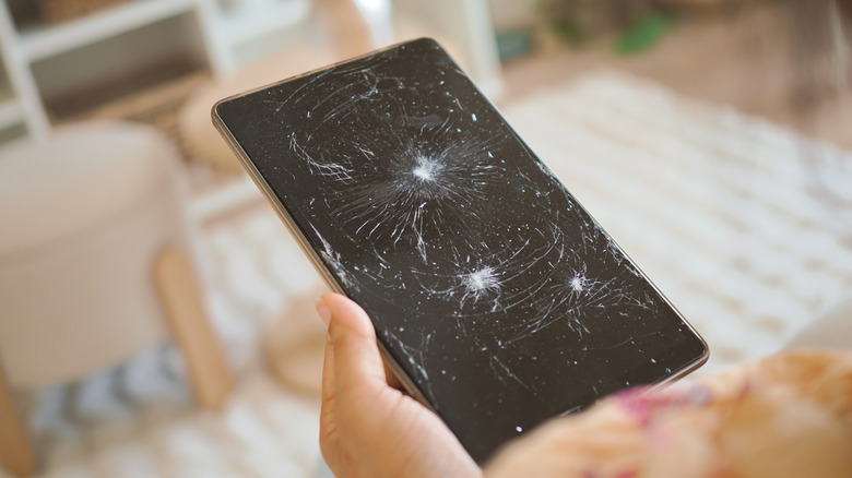 A tablet being held in a user's right hand, the screen on the tablet is severely damaged