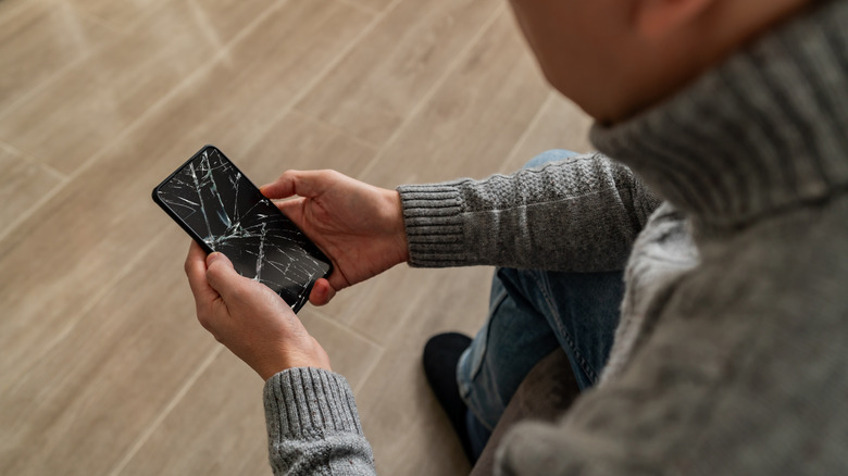 Looking over the shoulder at a phone with a cracked screen