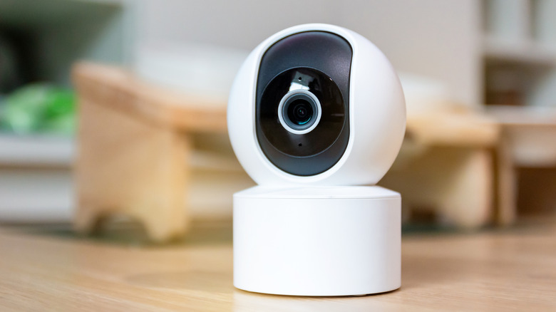 Small white indoor security camera with a central lens on a tabletop.