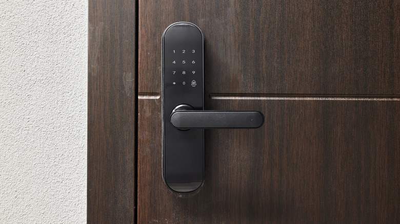 Black smart door lock with keypad installed on a dark wooden door.