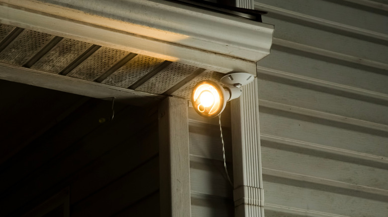 Outdoor security camera with built-in spotlight mounted under a house roof eave at night.