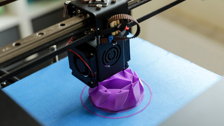 3D printer creating a purple geometric model on a blue print bed.