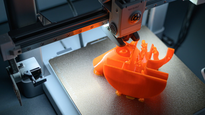 3D printer creating an orange model on its build plate.