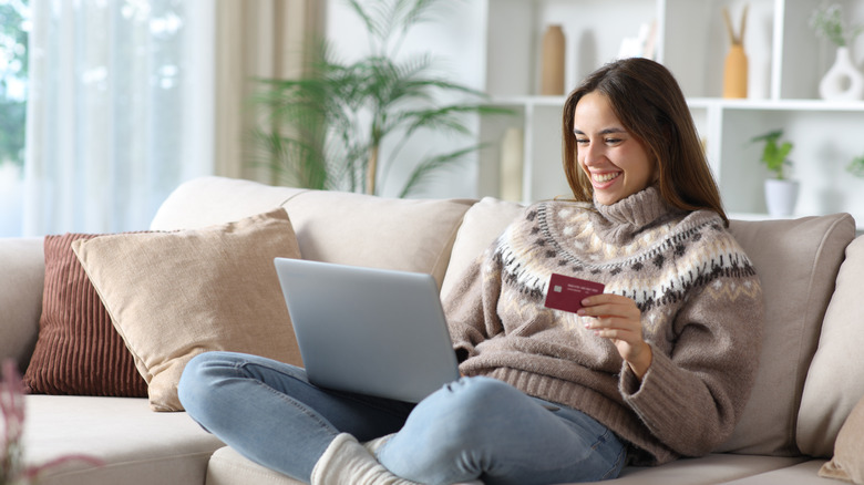 woman looking at laptop, holding credit card in winter clothing