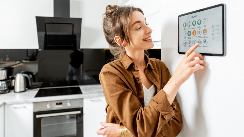 Woman using a wall-mounted smart home control panel in a kitchen.
