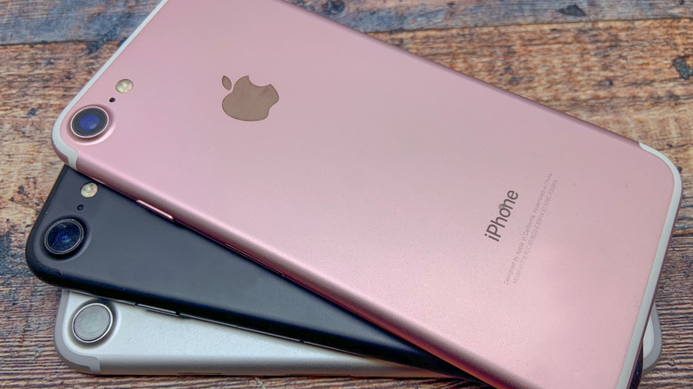 Stack of older iPhone models placed on a wooden surface.