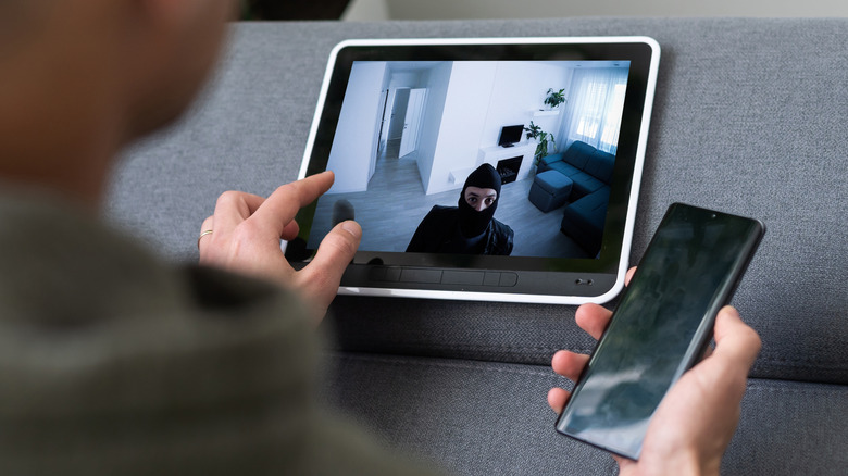 Person viewing a home security camera feed on a tablet while holding a smartphone.
