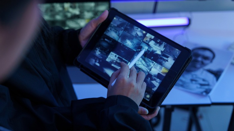 Person using a tablet to monitor multiple security camera feeds.