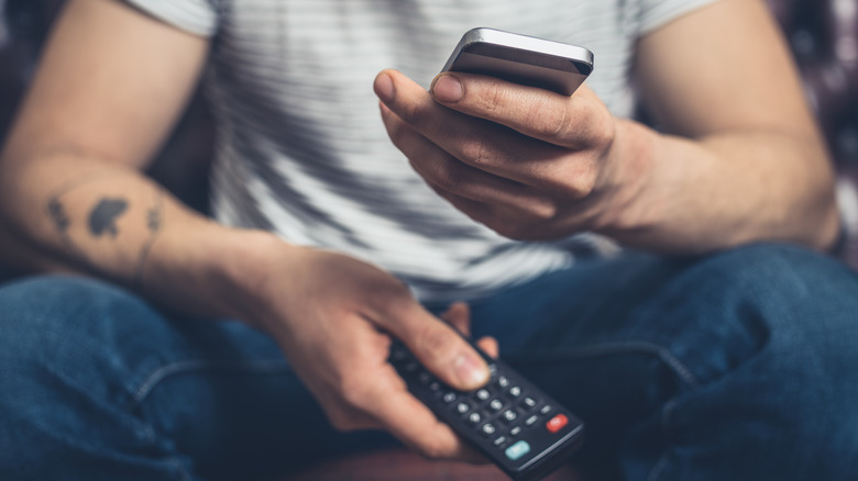 Person holding a smartphone and TV remote control.