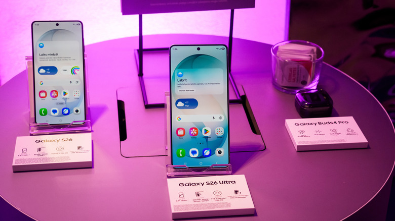 Samsung Galaxy S26 and S26 Ultra phones displayed beside Galaxy Buds under pink lighting.