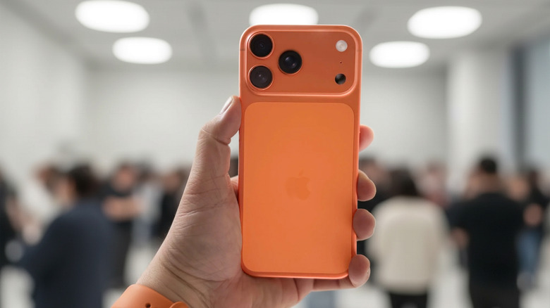 Person holding an orange iPhone 17 Pro Max with the rear cameras visible.
