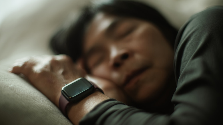 A person lying in bed with a square smartwatch on his wrist.