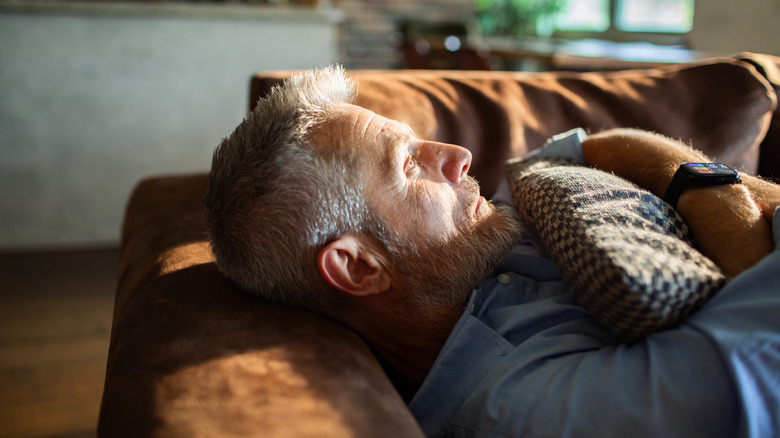 A person lying on the couch wearing a smartwatch and hugging a pillow.