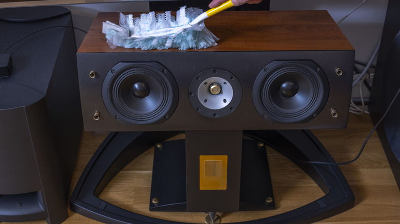 A hand dusting a speaker on a wooden table