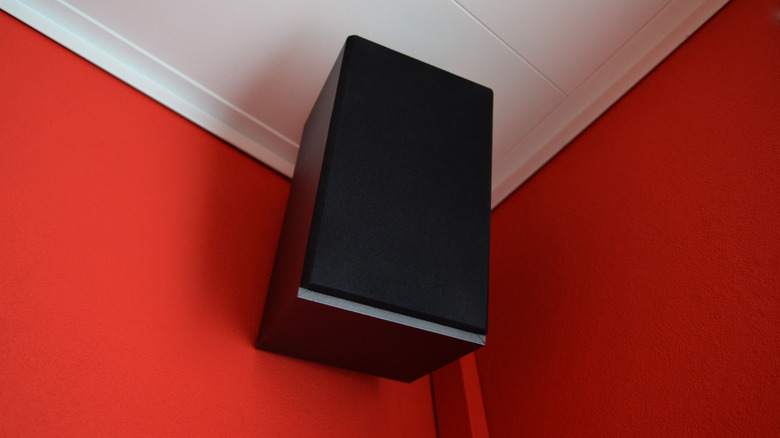 A speaker mounted on a red wall near the ceiling