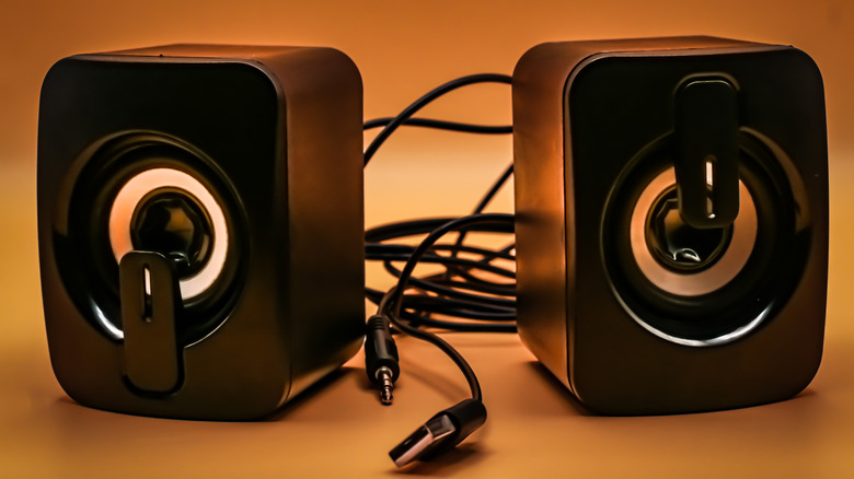A pair of mini speakers with cables against an orange background