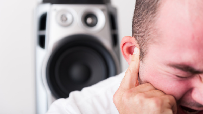 A person covering his ear due to loud volume from the speaker in the background