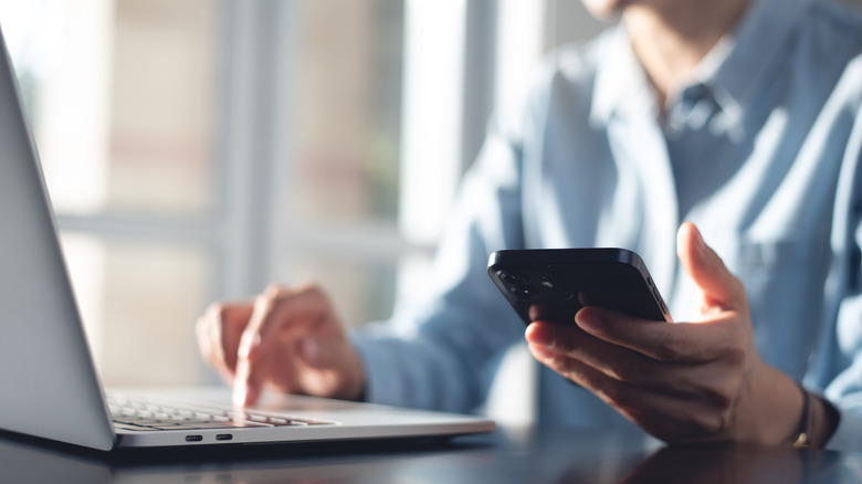 A man using his laptop while holding his phone in his hand