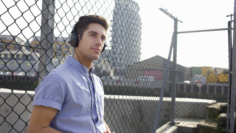 A man listening to music leaning against a fence
