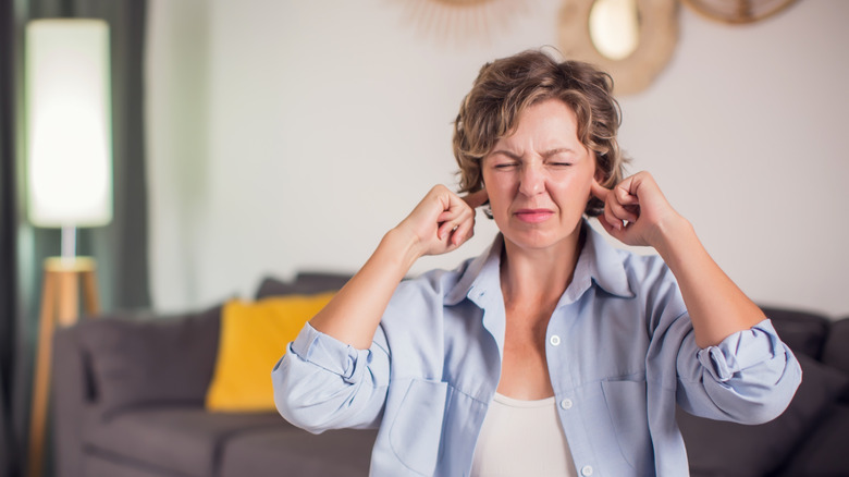 A woman plugging her ears with her fingers with an annoyed expression on her face