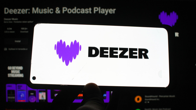 A phone showing Deezer logo with a Google Play Store screenshot in the background