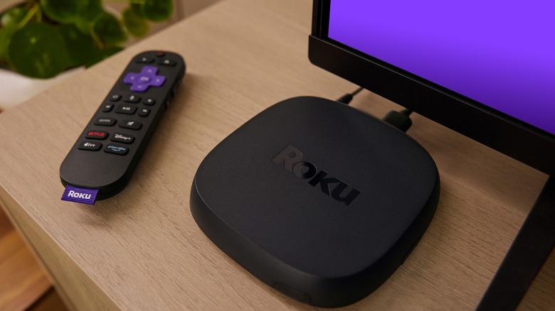 Roku Ultra streaming device next to remote and TV on wooden tabletop