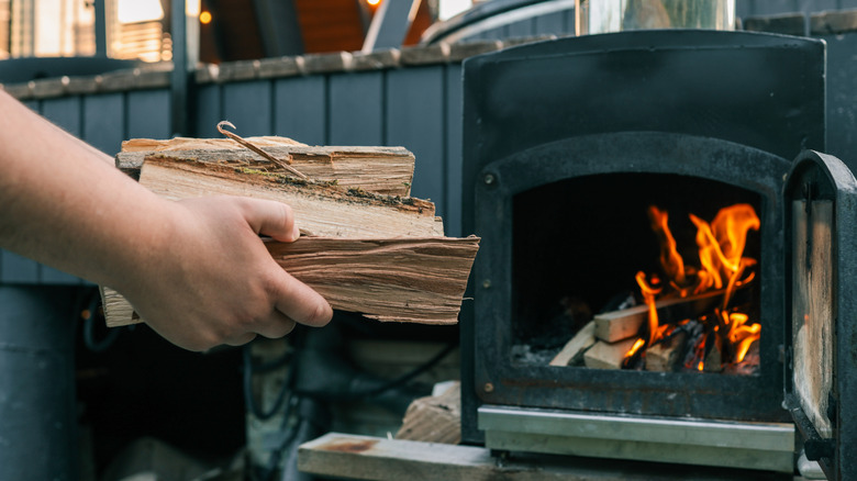 A person throwing logs into a stove.