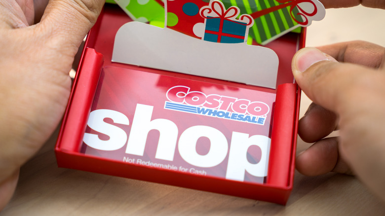 A pair of hands holding a Costco Shop card that's inside of an open gift box