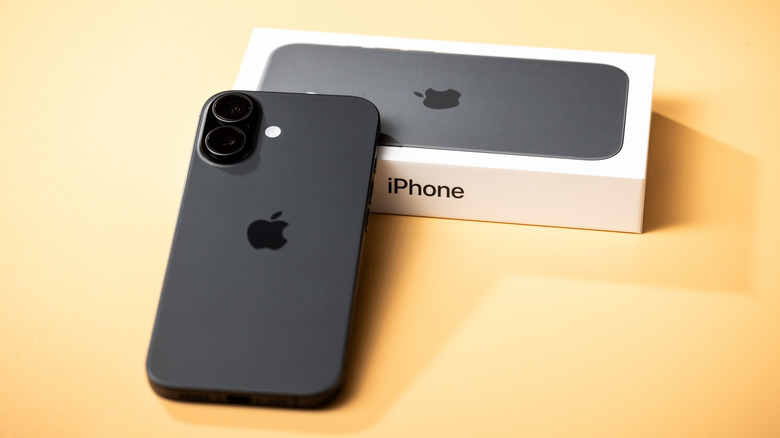 A black iPhone 17 with the top of the device resting against the box, both items are on a yellow backdrop