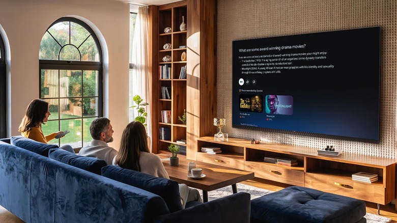 Three individuals are sitting on a blue couch and looking at a TV displaying information from Google Gemini
