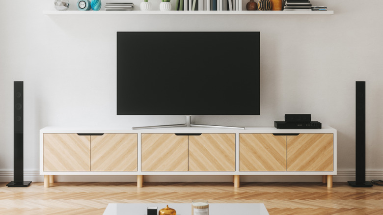 A small TV sits on top of a white TV stand with brown patterned shevles