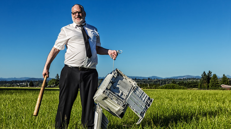 Person holding broken PC in field with baseball bat