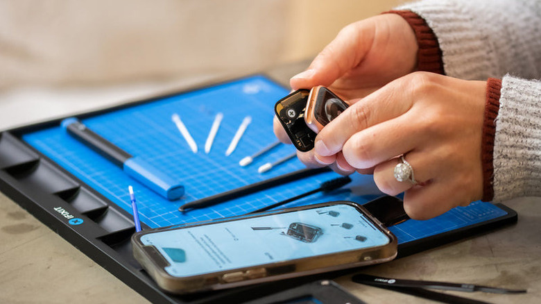 Hands using an iFixit FixMat while repairing small electronics.