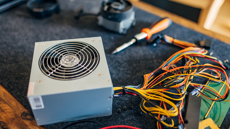 PC power supply with multicolored cables and repair tools on a workbench.