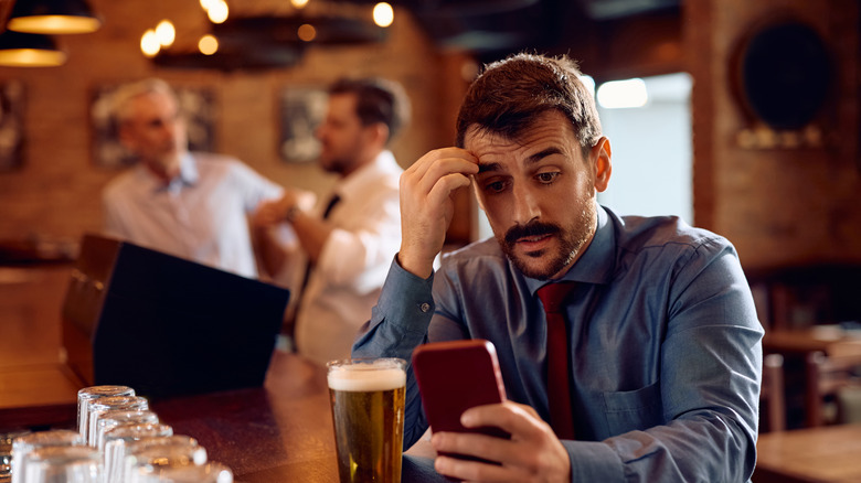Man looking at texts on a phone while enjoying a beer
