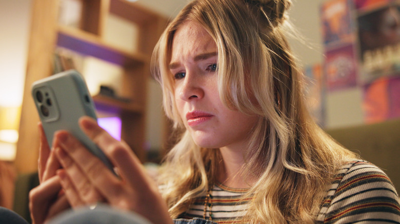 Distressed woman looking at phone as if having just received bad news in a text