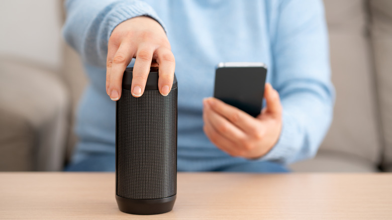 person connecting a smartphone to Bluetooth speaker placed on a wooden desk