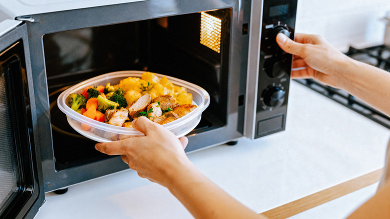 person putting a bowl of vegetables in a microwave oven